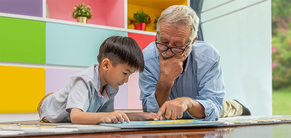 An elderly man reading with a preschool age boy.